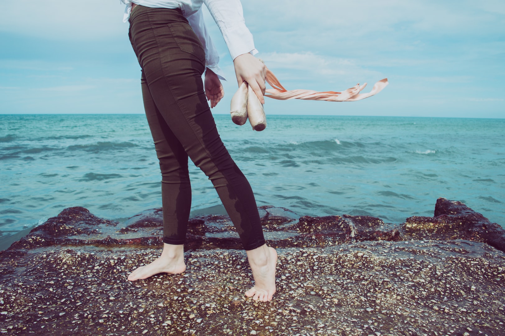 Barefoot woman on beach holds ballet shoes